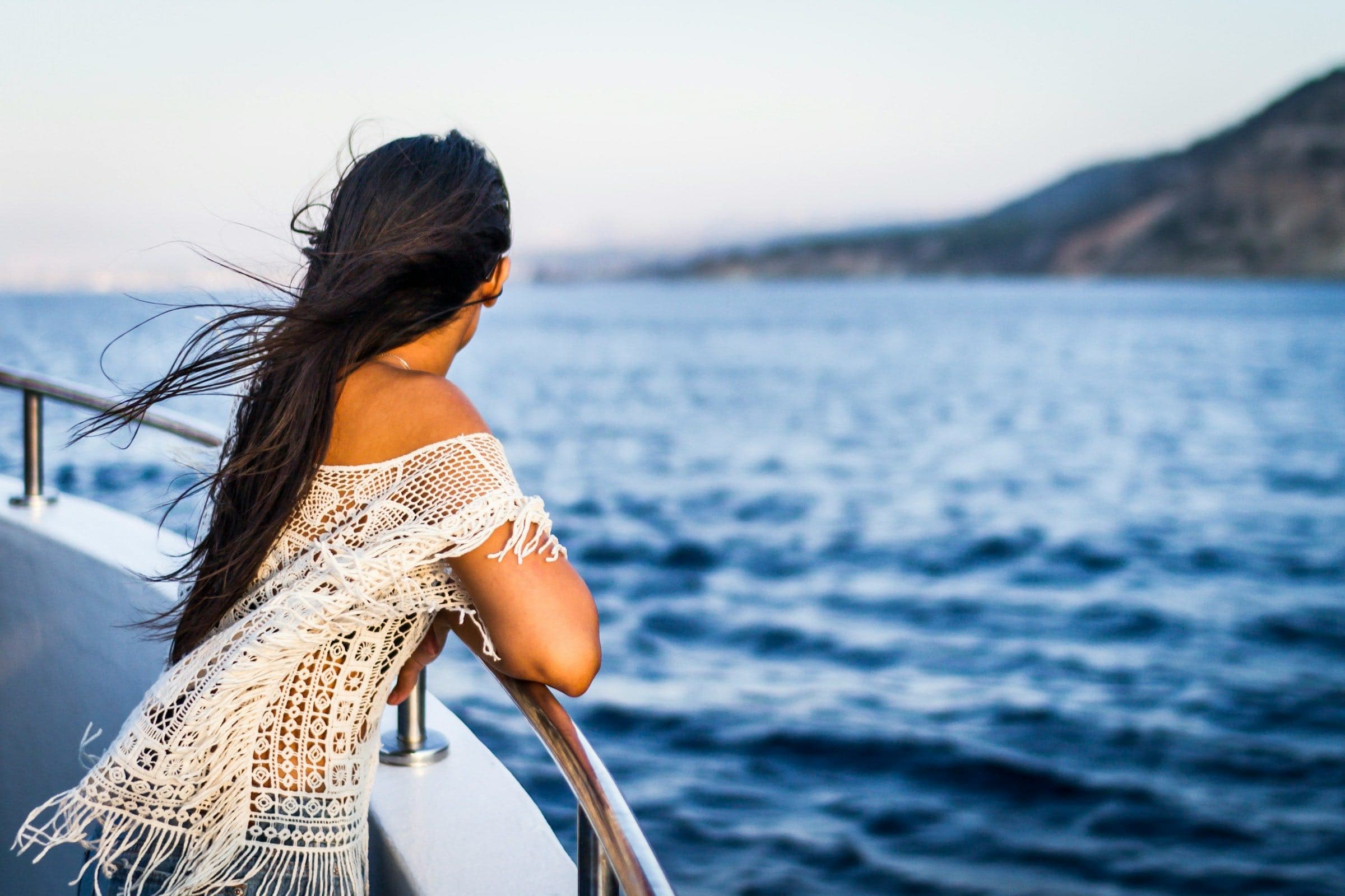 A woman at a boat rail above a deep blue sea at dusk
